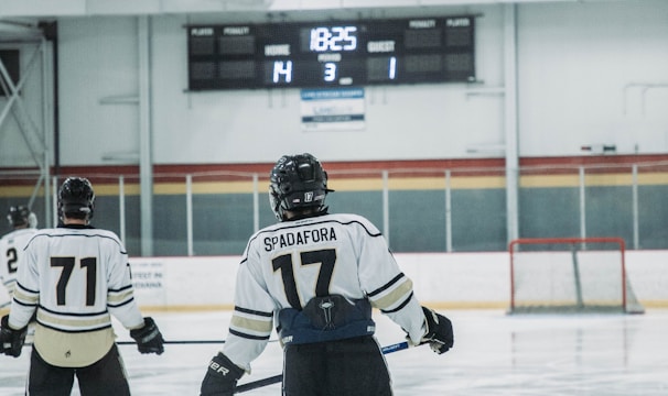 Two hockey players are on an ice rink, one with the name 'Spadafora' and number 17 on their jersey, and another with number 71. The score displayed on the scoreboard is Home 14, Guest 1, with the period indicated as 3 and the remaining time as 18:25.